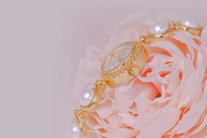 Detail of luxury gold watch with pearl bracelet band set on a soft pink flower