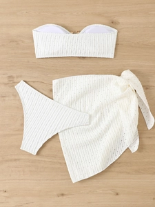 Flat lay of white three-piece bikini set with textured wavy fabric on wood background