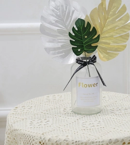 Detail of artificial monstera leaves in gold, silver, and green within a glass vase