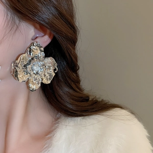 Close-up of a large textured silver metallic flower earring worn by a model