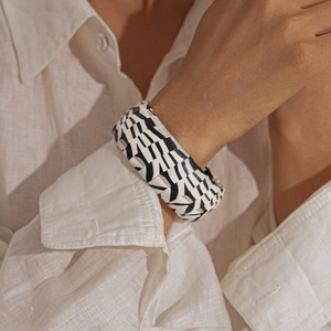 Macro detail of a wide black and white geometric pattern cuff bracelet on a white sleeve