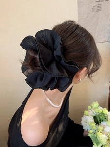 Detail of a large black ruffled fabric scrunchie styled in hair with a floral design