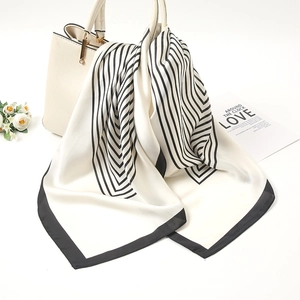 Detail view of a black and white striped silk scarf tied elegantly on a cream handbag