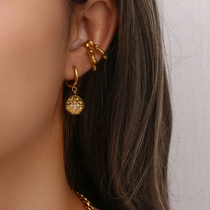 Close-up of gold starburst hoop earrings and textured ear cuff on model