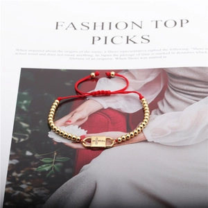 Adjustable red rope bracelet with gold cross pendant and zircon beads on magazine background