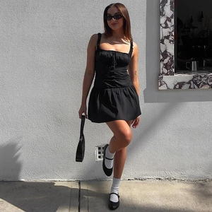 Slim fit black mini dress with button details and pleats shown in an outdoor street style