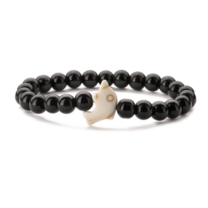 Detail shot of a black polished beaded bracelet with a white dolphin-shaped centerpiece
