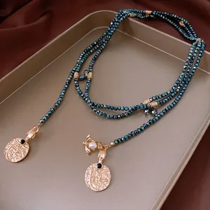 Vintage triple-layer green beaded necklace with gold coin pendants on a satin background