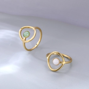 Elegantes anillos dorados con perlas de concha en verde y blanco sobre fondo texturizado ondulado