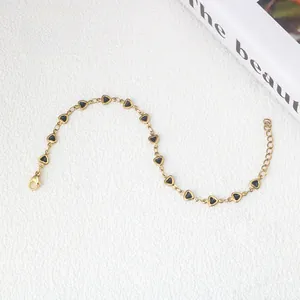 Dettaglio di un bracciale dorato con piccoli cuori in smalto nero e chiusura a moschettone