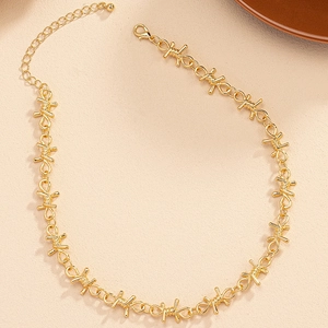 Detail of a gold thorn-style chain necklace with barbed wire knots on a beige surface