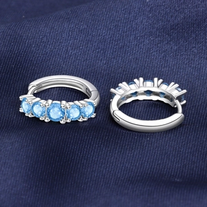 Détail de créoles en argent serties de cinq pierres bleu clair sur un tissu bleu foncé