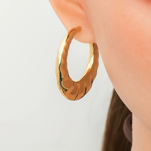 Detailed view of large gold hoop earring with wave texture worn by a model