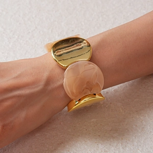 Vista dettagliata di un ampio bracciale in metallo dorato e resina marmorizzata rosa