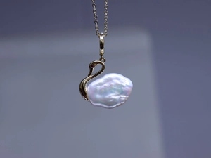 Gros plan du collier cygne avec perle baroque irisée et détails en métal doré