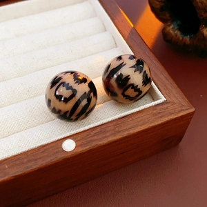 Detail of round leopard print stud earrings on a vintage leather and wood jewelry display