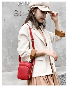 Detail of a red nylon crossbody bag with multi-layer zippers and adjustable strap