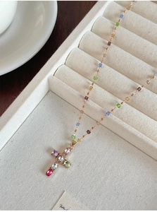 Détail macro du collier croix doré avec zircons colorés et perles de cristal