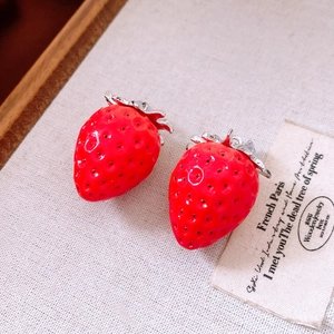Close-up of red strawberry pendants with silver hardware on a vintage fabric background
