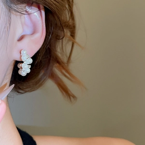 Detailed view of silver needle pearl earrings with crystals on a golden base
