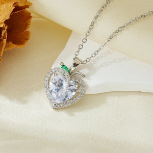 Macro detail of heart-shaped silver pendant with clear zircon and green stone accent