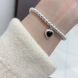 Detailed shot of a silver beaded bracelet with black heart charm worn on a wrist