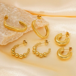 Detailed view of three 18K gold plated stainless steel C-shaped earrings on satin fabric
