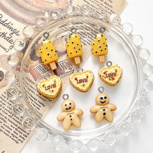 Macro detail of resin heart cake, ice cream, and gingerbread man DIY charms in a glass dish