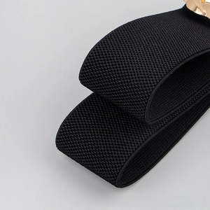 Macro detail of elastic black woven fabric and gold metal buckle on a wide waist belt