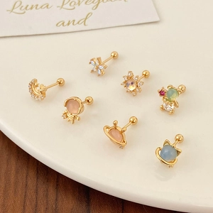 Golden stud earrings set with zircon moon and planet designs on white display plate