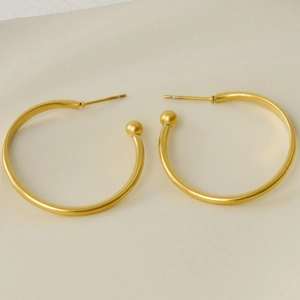 Minimalist 304 stainless steel gold-finish hoop earrings with ball ends on beige surface