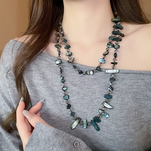 Detail of layered iridescent shell and crystal beaded necklace on a grey sweater