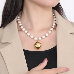 Detail of elegant pearl necklace with a polished gold hollow sphere pendant on a model