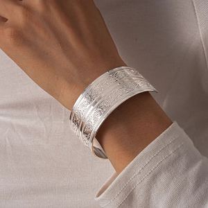 Detailed view of the intricate floral engraving on a wide silver-tone open cuff bracelet