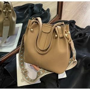 Detailed close-up of khaki pebbled leather bucket bag with woven strap and gold hardware