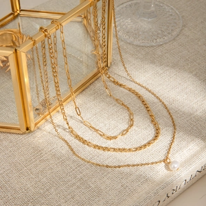Detail of layered gold stainless steel necklace with pearl pendant on glass box
