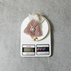 Detail showing the 12g weight of a pink plush angel Christmas tree ornament on a scale