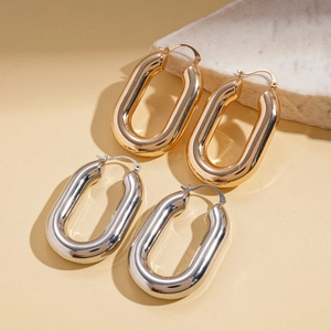 Minimalist oval metal hoop earrings in gold and silver finishes on a stone display