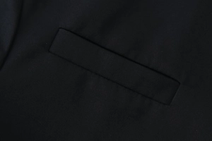 Close-up of a precision-crafted welt pocket on black twill textured blazer fabric
