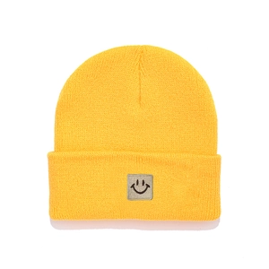 Close-up of a vibrant yellow knit beanie with a stylish grey square smiley face patch