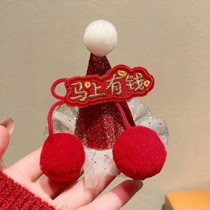 Detail of red festive hat hair clip with gold embroidery and soft white pom-poms