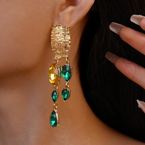 Detail view of model wearing vintage geometric teardrop earrings with green and gold stones