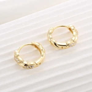 Twisted gold vermeil huggie earrings with cubic zirconia stones on white textured surface
