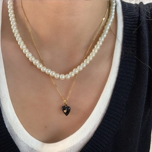 Double-layered gold necklace featuring white pearls and a black heart-shaped pendant