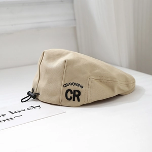 Macro detail of beige cotton kids beret showing CR embroidery and adjustable drawstring