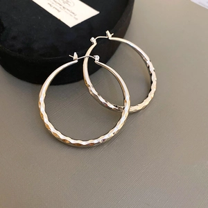 Macro shot of silver faceted hoop earrings with geometric textures on a grey background