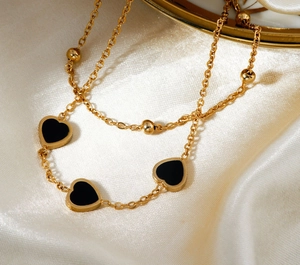 Detailed close-up of golden chain necklace with black heart charms on white silk fabric