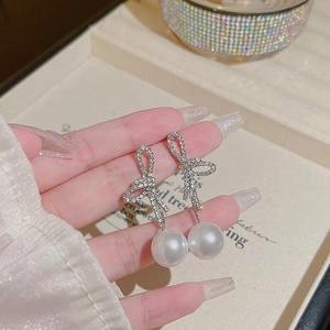 Detailed close-up of silver bow earrings with sparkling rhinestones and white pearls
