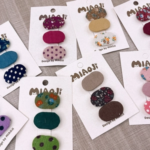 Dettaglio di tre fermagli ovali in tessuto con motivi floreali e pois su cartoncino