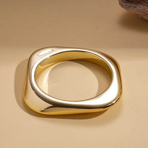 Macro view of minimalist irregular geometric gold cuff with polished mirror finish